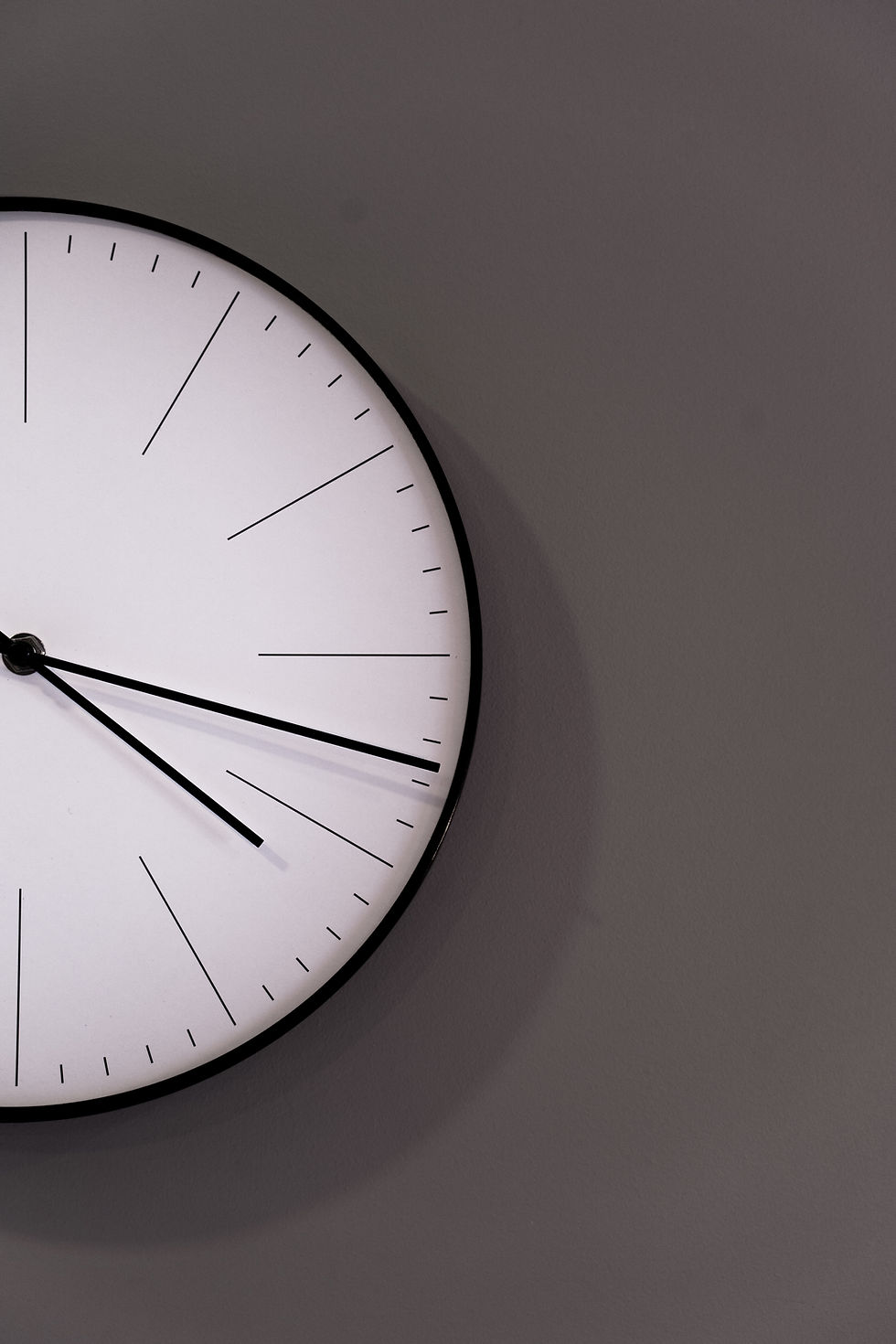 A minimalist analog clock on a gray wall, the picture for "Pemuda legasi malaysia baharu", an essay by Muhamad Hazman bin Norhamzah