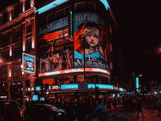 In the theatre district, a large neon banner of the musical Les Misérables lights the dark.