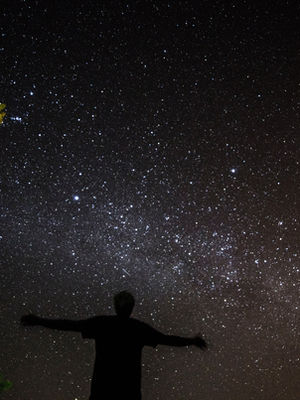 A person with their arms out looking up at a night sky showing millions of stars
