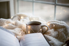 a mug on a blanket with a book and fairy lights