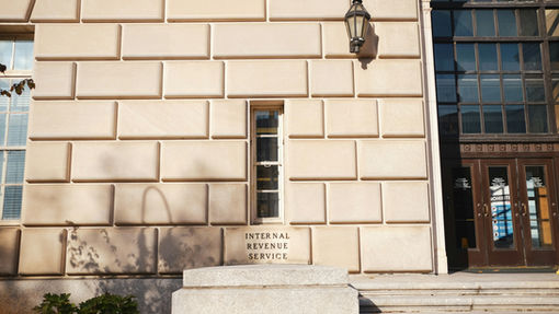 IRS building exterior with American flags representing how S Corp taxes work, including S Corporation tax reporting, IRS compliance, Form 1120-S filing, and shareholder tax requirements.