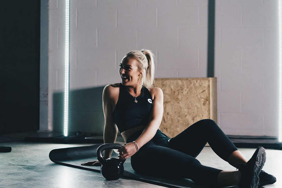 A woman who has just completed a 10 minute kettlebell workout. She is sitting a CrossFit gym holding a 1 pood kettlebell.