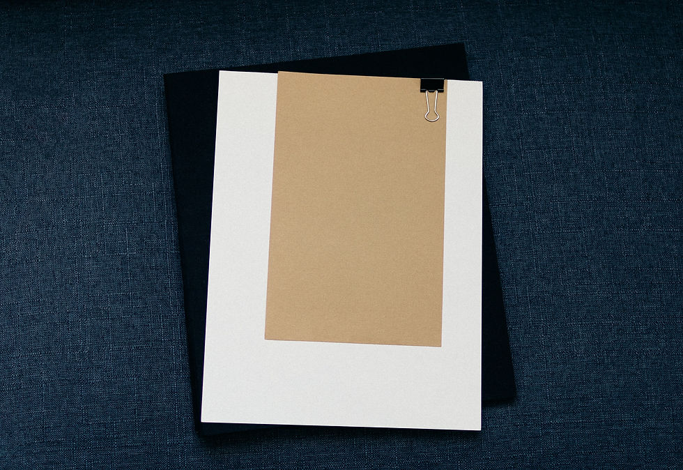 Blank white and tan papers clipped over a black sheet on blue denim, a neat minimalist stationery layout.