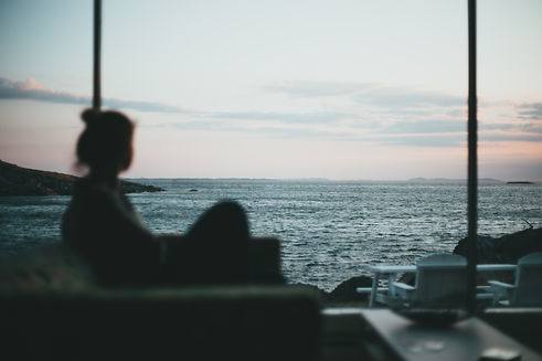 person sat in a state of calm on a couch looking out of a window at the ocean