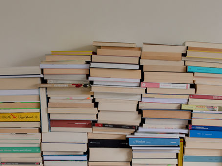 Stacks of paperback books piled against a plain wall, with colorful spines and visible titles like Harry Potter and Wenders.