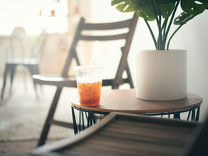 Sunlit table with a potted plant and a drink beside an empty chair, creating a peaceful and uncluttered space for quiet reflection.