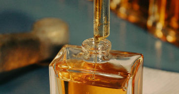 Gloved hand filling a square glass perfume bottle with amber liquid