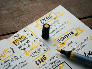 Open notebook with handwritten notes in black and yellow ink, featuring motivational text. A yellow highlighter and cap rest nearby on a wooden surface.