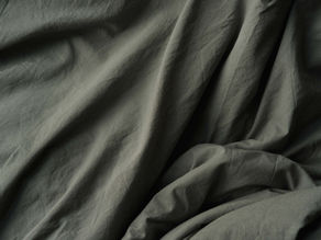 A close-up of wrinkled, grey bedsheets with creases and black shadows.