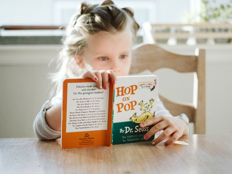 a young child sitting at a table reading the book Hop on Pop