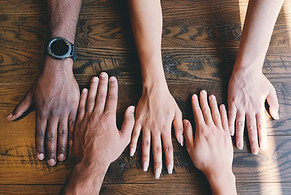 Five hands of people from different races and genders on a woden table.