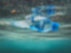 Plastic bottle floating underwater in a blue-green sea with visible bubbles and particles. Environmental pollution theme.