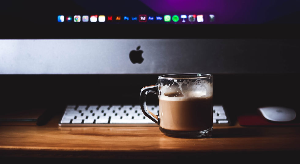 Bilgisayar masasında çalışma yapmaya hazır olan Apple marka iMac model masaüstü bilgisayar ve bir fincan sütlü kahve duruyor.