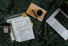 Personal tax preparation workspace with tax forms, a calculator, laptop, notebook, and cup of coffee.