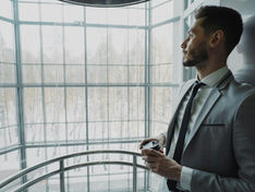 Male leader in professional attire standing alone at office window, representing the hidden psychological pressure carried by leaders as an unmanaged psychosocial risk.
