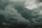 Dark storm clouds fill the sky, with a bright opening in the upper right and a brooding, dramatic mood.