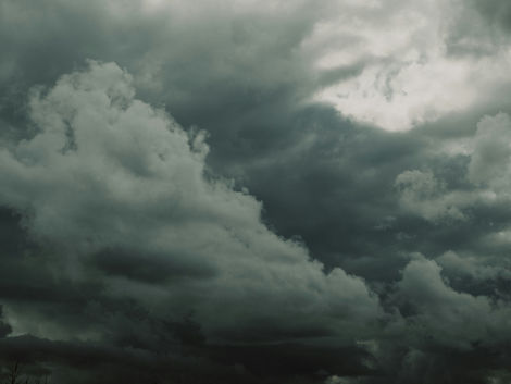 Dark storm clouds fill the sky, with a bright opening in the upper right and a brooding, dramatic mood.