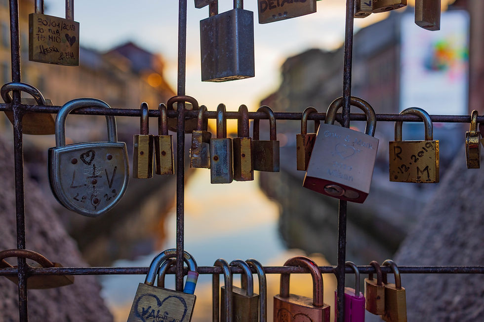 Multiple padlocks of different sizes hanging from a fence overlooking a river.
