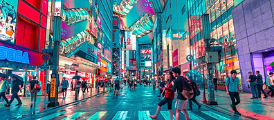 A busy street scene in a Japanese city at night, filled with people walking under bright neon lights and colorful signs. Reflections shimmer on the wet pavement, creating a vibrant, lively urban atmosphere.