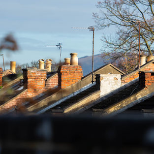 Row of brick rooftop chimneys and TV antennas under a clear blue sky, with bare trees in the background.