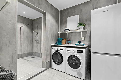 Modern laundry room with white washer and dryer, concrete walls, refrigerator, and an adjoining open shower area
