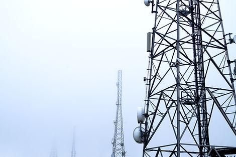 Steel telecommunication towers in misty setting, with overcast sky. Structures feature complex metal frameworks and round antennas.