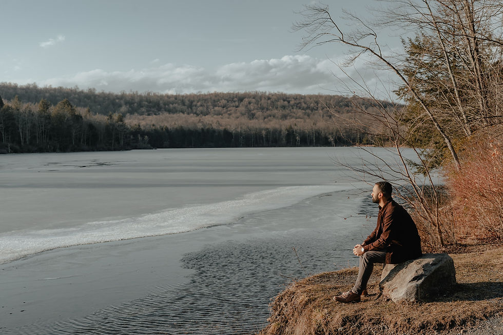 A man sitting on a rock looking out a lake and forest