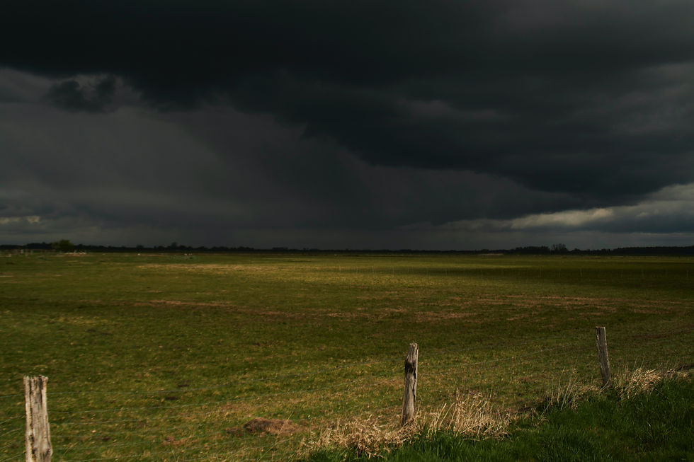 Black storm clouds in distance, green field and fence posts in foreground