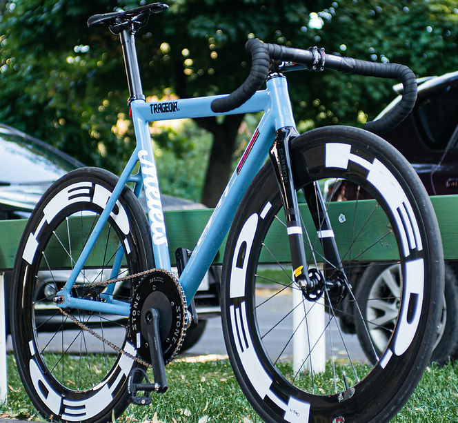 Blaues Fahrrad mit Aufschrift, Fahrradrahmen, vor Bäumen und Wagen, Vagabundo