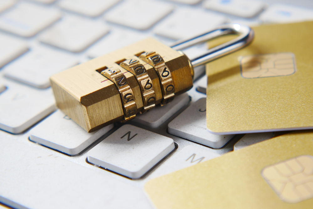 Protected padlock resting on two credit cards with chips and a keyboard.