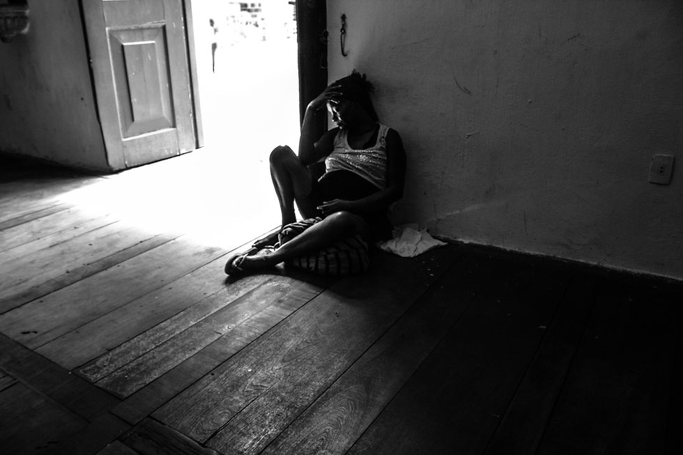 A silhouette of a person sitting against a wall in a dimly lit room, head in hand, near an open door with bright light outside, creating a somber mood.