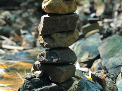 Stacked stones in a forest setting, with sunlight filtering through leaves. Natural, earthy tones set a peaceful, balanced mood.