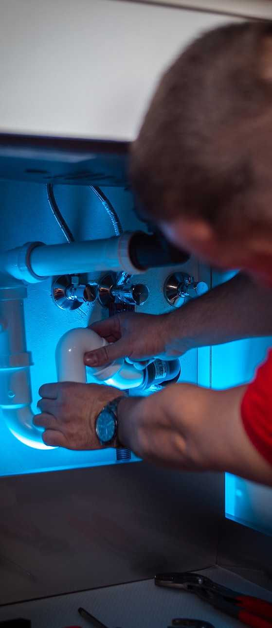 Plumber repairing white pipes under a kitchen sink