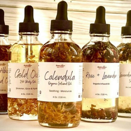 Five amber dropper bottles of infused oils with flowers inside, labeled Rose+Hibiscus, Gold Oil, Calendula, Rose+Lavender, Lavender+Chamomile